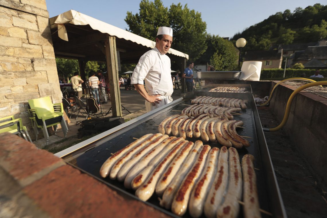 Saucisses en train de griller à la braise au restaurant de groupes Les Tablées de L'Oustal en Aveyron