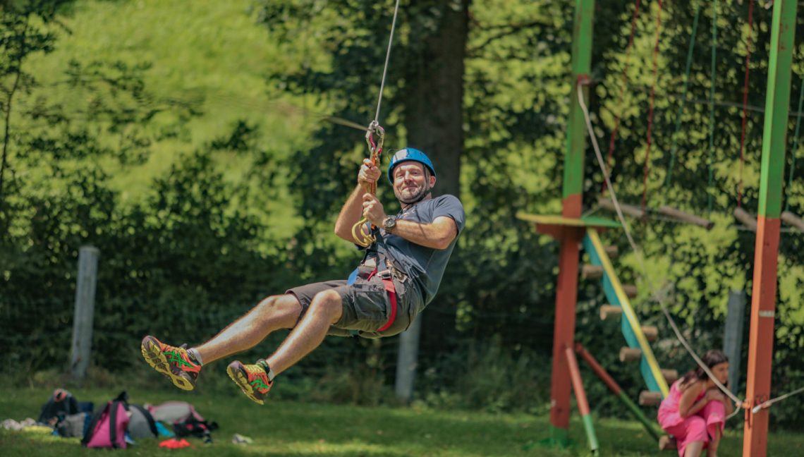 Adulte en pleine descente de tyrolienne au parcours accrobranche du parc aventure de la vallée de Vanc à L'Oustal Pont-les-Bains en Aveyron